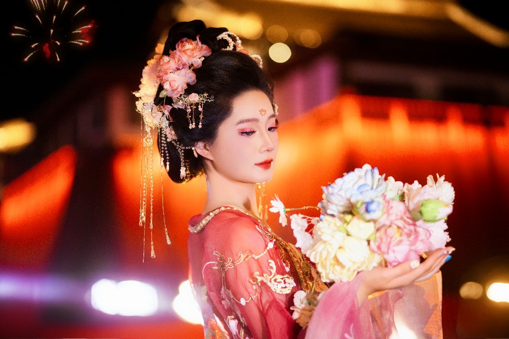 穿粉色汉服、手捧鲜花的女生站在大唐不夜城的夜景灯光里